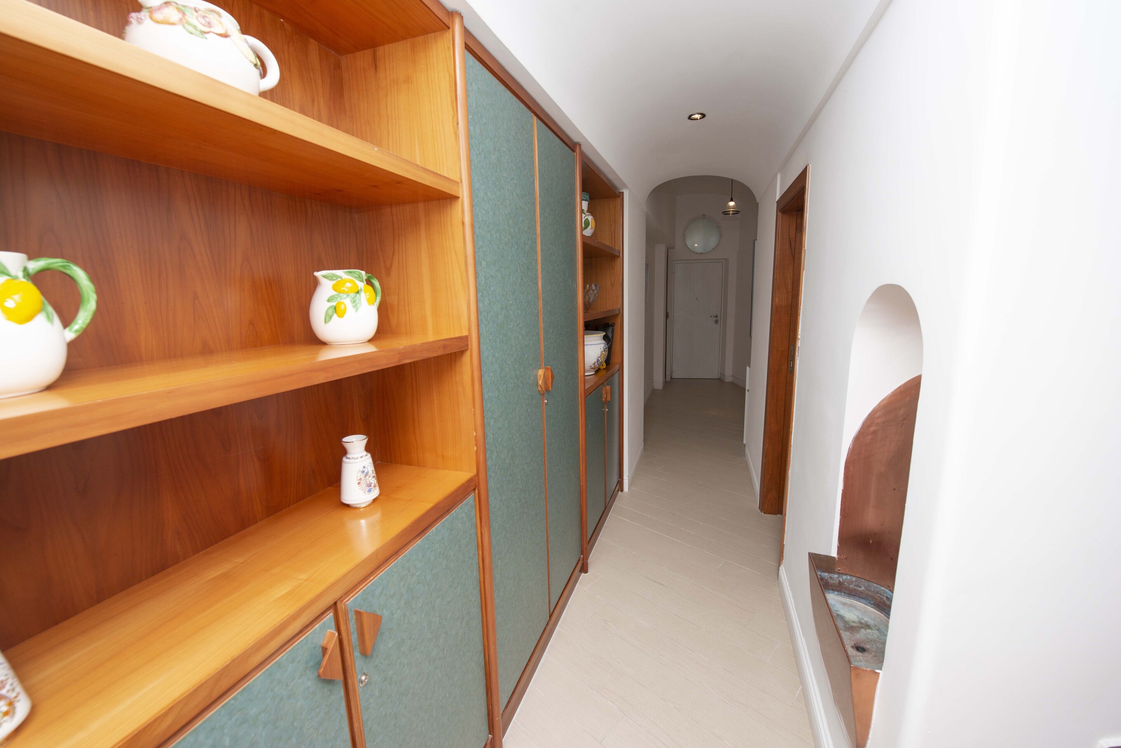 Un couloir avec des étagères et des armoires en bois, une porte au fond et un plancher de couleur claire.