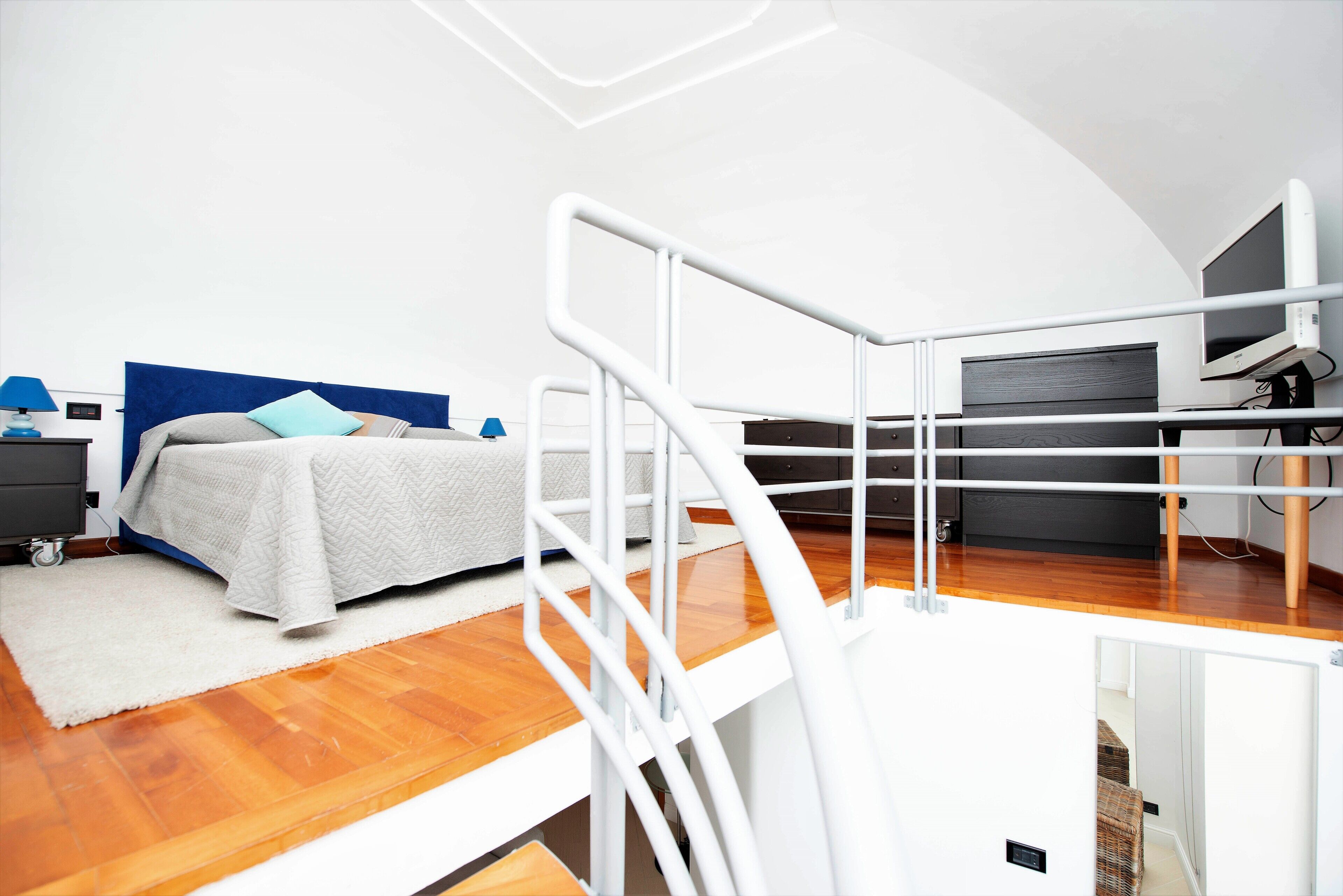 A bedroom with a bed, bedside tables, a desk, and a TV.