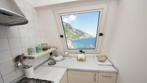 A kitchen with a gas stove, a window with a view of the sea, and a shelf with kitchen items. - Casa Margherita ..... Positano, perfect location for your holiday in Positano (Positano)