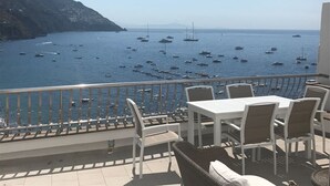 A terrace with white tables and chairs overlooking a coastal area with boats and a hilly landscape. - Casa Margherita ..... Positano, perfect location for your holiday in Positano (Positano)