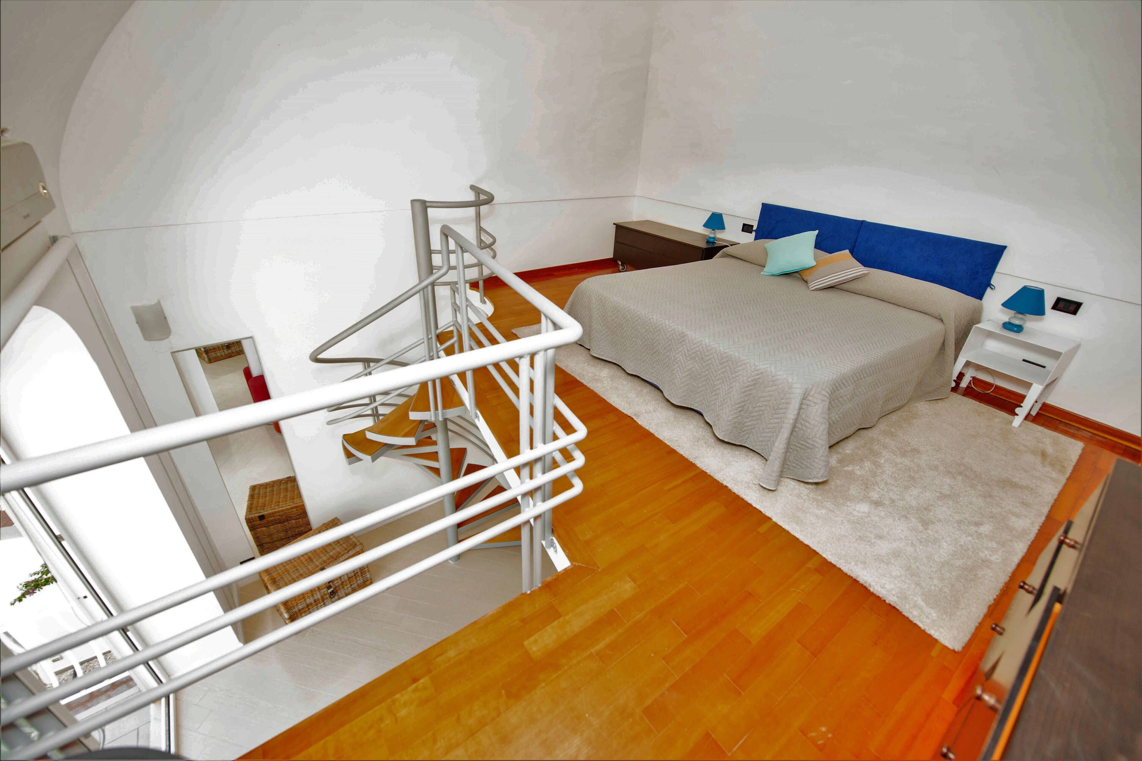 A bedroom with a bed, nightstands, a white railing, and a wooden floor.