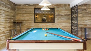 Un tavolo da biliardo con una parete di legno a fare da sfondo, un lampadario sospeso e uno specchio decorativo sopra.