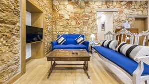 Una stanza con parete in pietra, un divano blu, un tavolino in legno e un televisore fissato al muro.