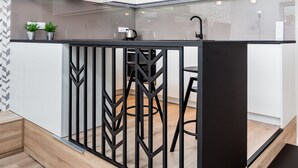 A modern kitchen with white cabinets, a black countertop, and a black island with bar stools. - VISENTO Apartments Kreta 52-54 (Bialystok)