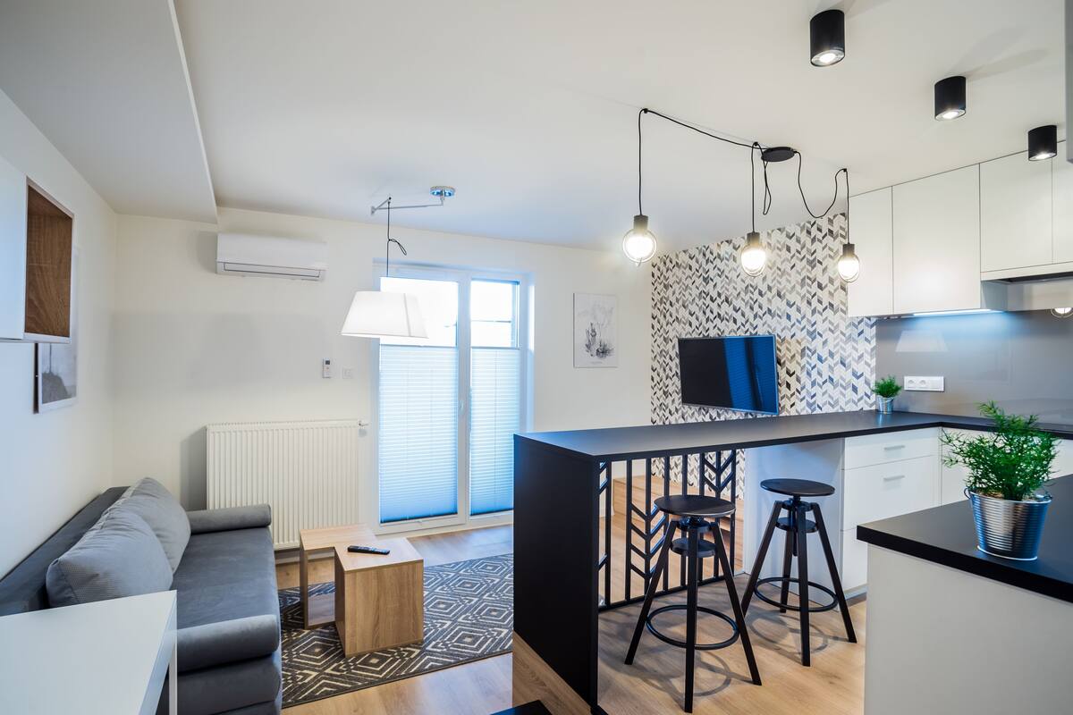 Une cuisine moderne avec un îlot central noir, des tabourets de bar, des luminaires suspendus et un pare-feu décoratif.