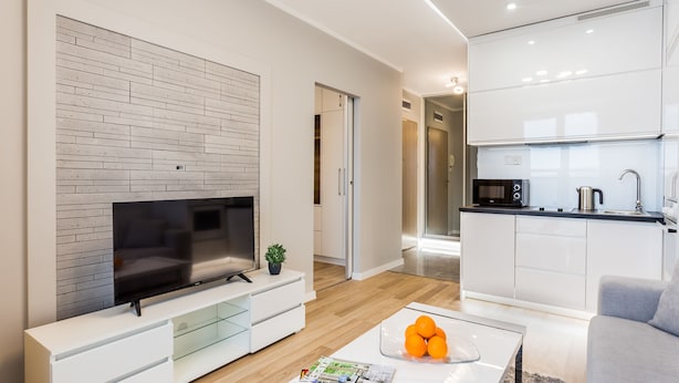 A modern living room with a flat-screen TV, a coffee table with magazines, and a kitchen area with white cabinets and a microwave. - VISENTO Apartments Kreta 52-54 (Bialystok)