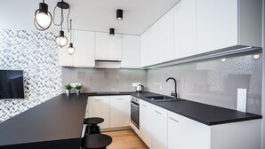 A modern kitchen with white cabinets, a black countertop, and pendant lighting. - VISENTO Apartments Kreta 52-54 (Bialystok)