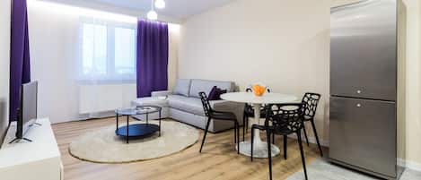 Una sala de estar moderna con un sofá, una mesa de comedor con sillas, un refrigerador y un televisor sobre un mueble.