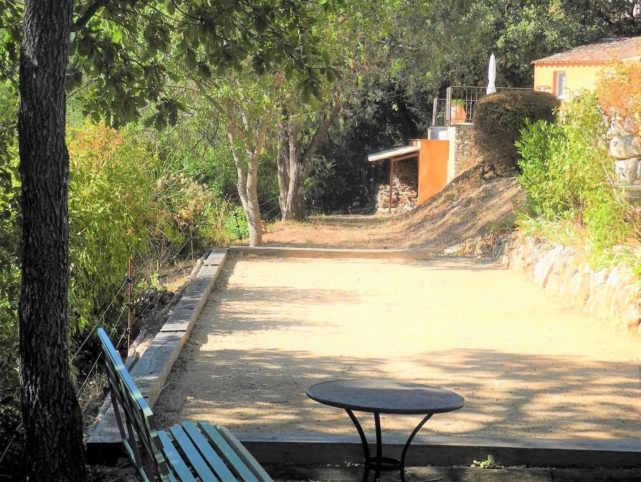 A paved area with a bench and a table, surrounded by trees and a stone wall.