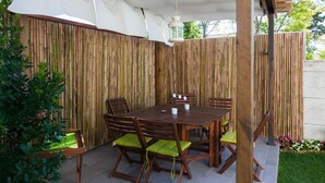 A covered patio area with a wooden table and chairs, surrounded by bamboo walls.
