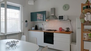 A modern kitchen with white cabinets, a wooden countertop, a gas stove, a microwave, and a refrigerator. There is a window with a view of buildings outside.