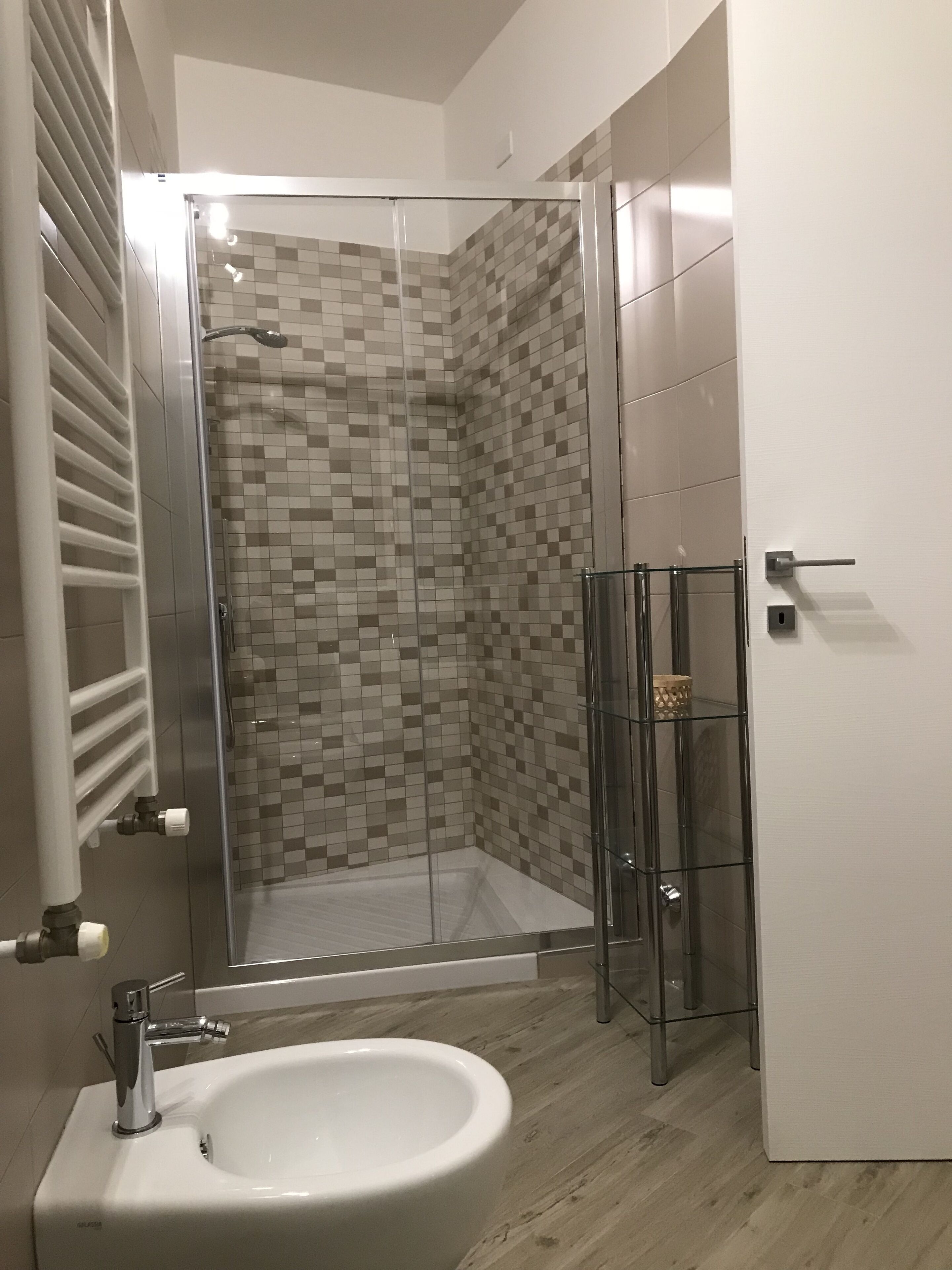 Une salle de bain moderne avec une douche à parois de verre, un lavabo blanc et un mur de douche recouvert de carreaux.