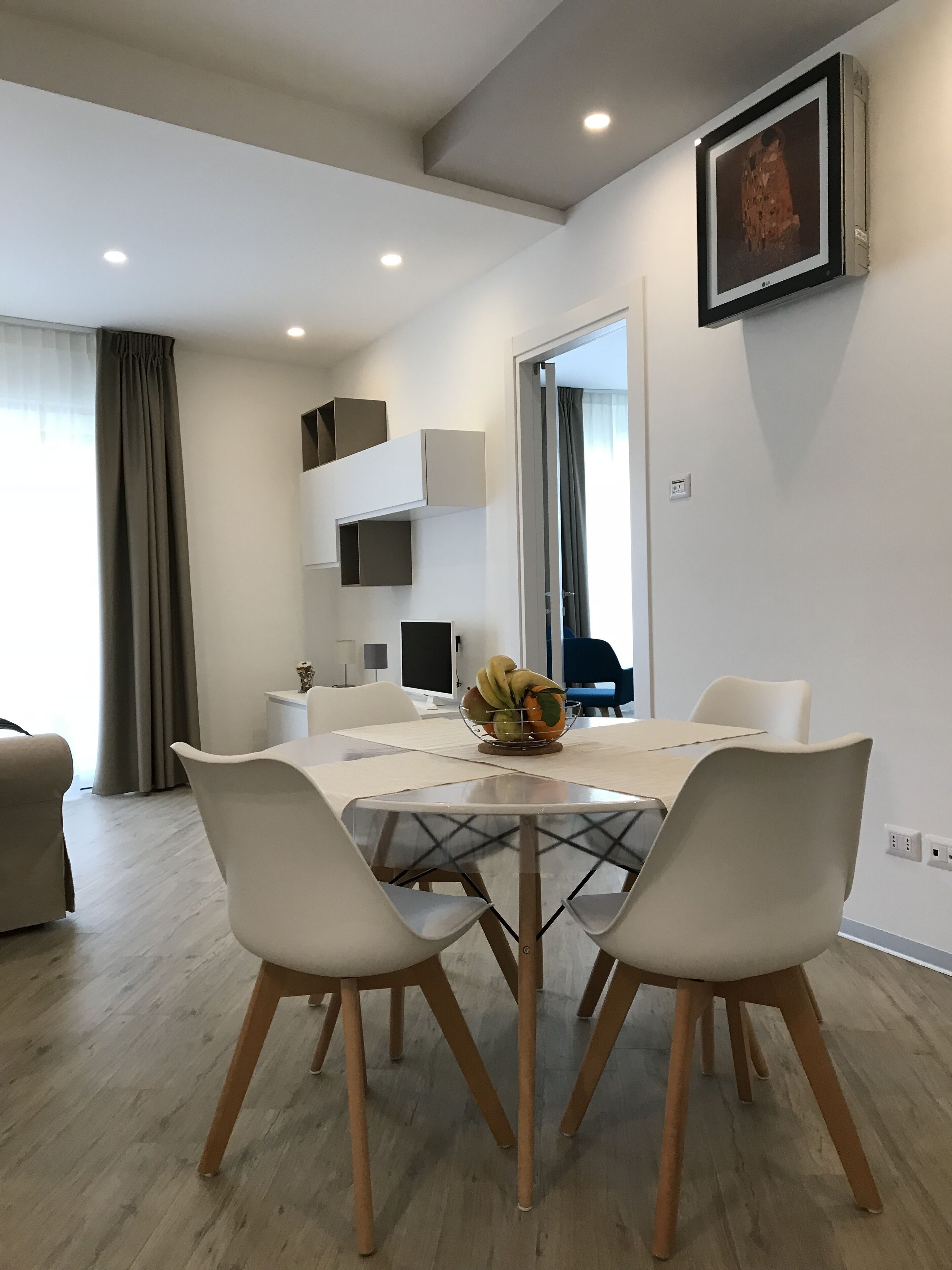 A modern living room with a dining area, featuring a dining table with chairs, a TV, and a framed artwork on the wall.