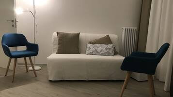 A room with a white sofa, two blue chairs, and a floor lamp.