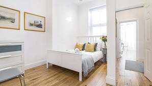A bright, white room with a bed, a desk, and a chair. There are two framed pictures on the wall. - Luxury 2 Bed apartment- Zone 2 ( 10 mins into Central London)  (London)