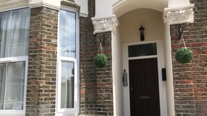 A brick building with a white door, a small porch, and a window with a curtain. - Luxury 2 Bed apartment- Zone 2 ( 10 mins into Central London)  (London)