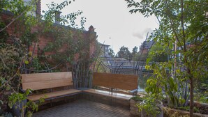 A bench in a garden area with brick flooring and potted plants.