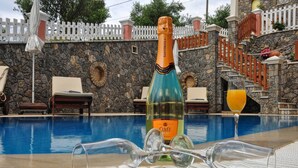 Ein Poolbereich mit einer Cuvée-Champagnerflasche, einem Glas Orangensaft und leeren Weingläsern auf Liegestühlen.