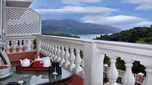 Ein Balkon mit Glastisch, weißer Brüstung und einem schönen Blick auf Berge und einen See.