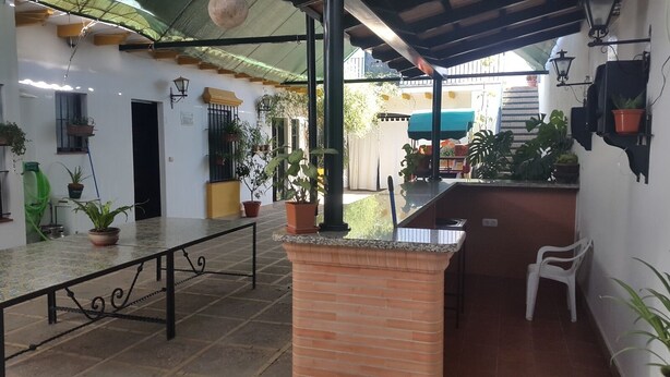 A covered outdoor area with a tiled floor, a metal table, potted plants, and a small white chair. - Beautiful house rociera to enjoy with your people (El Rocío)