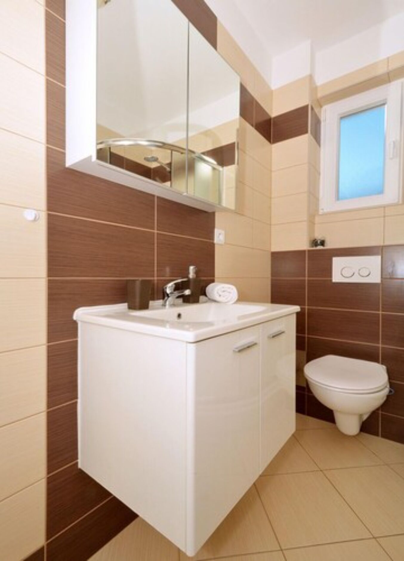 A bathroom with a white vanity, a mirror, a toilet, and a window.