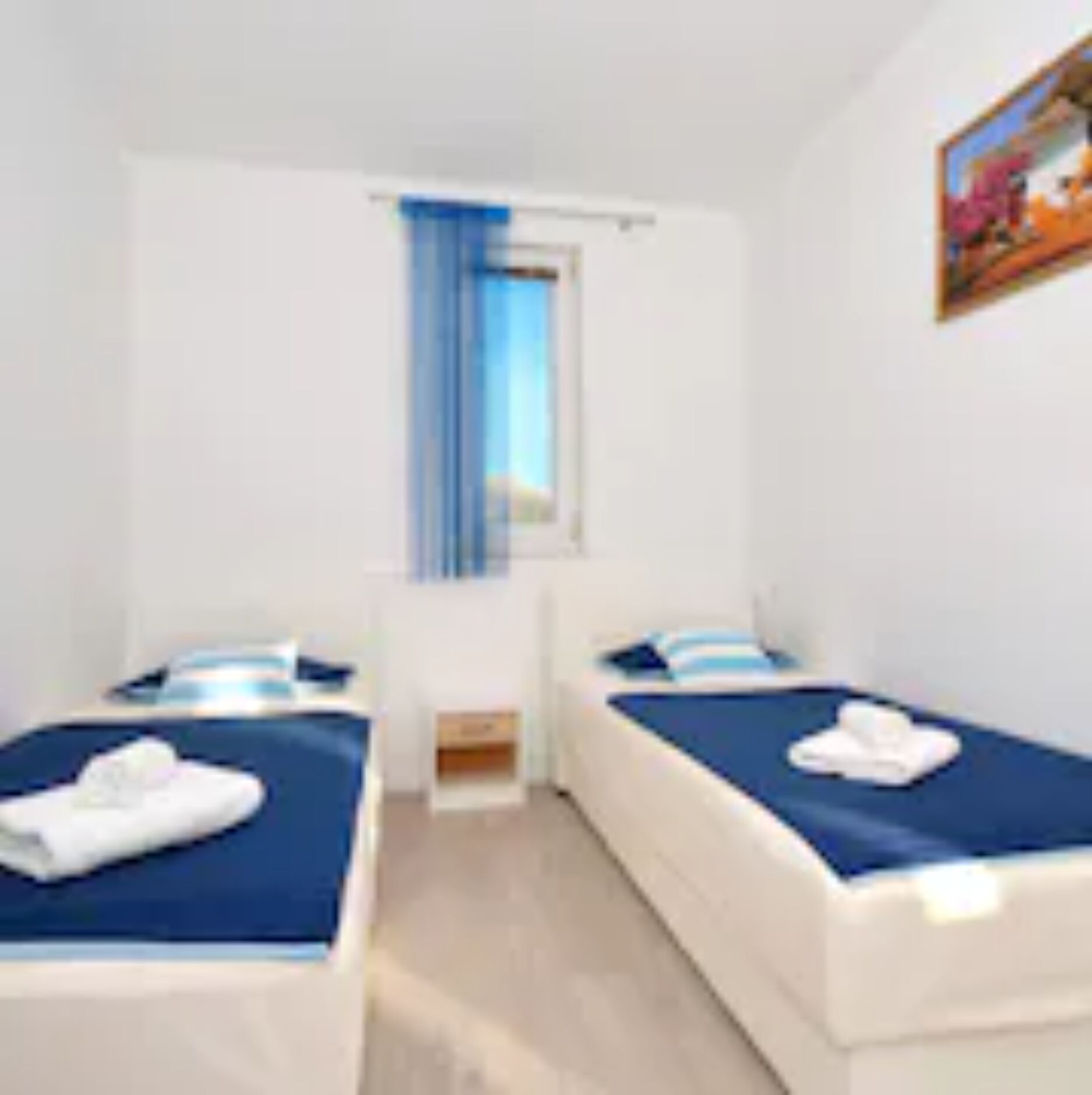 Una habitación con dos camas, una ventana con cortinas azules y un cuadro en la pared.