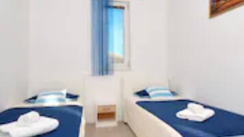 Una habitación con dos camas, una ventana con cortinas azules y un cuadro en la pared.