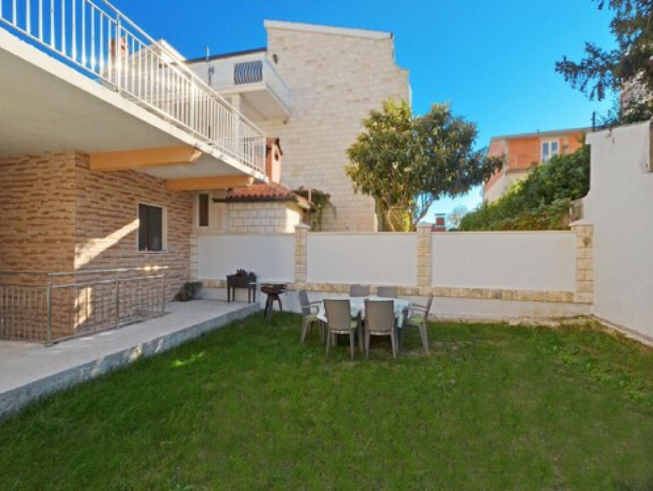 A two-story building with a balcony, a small patio area with outdoor furniture, and a well-maintained lawn.