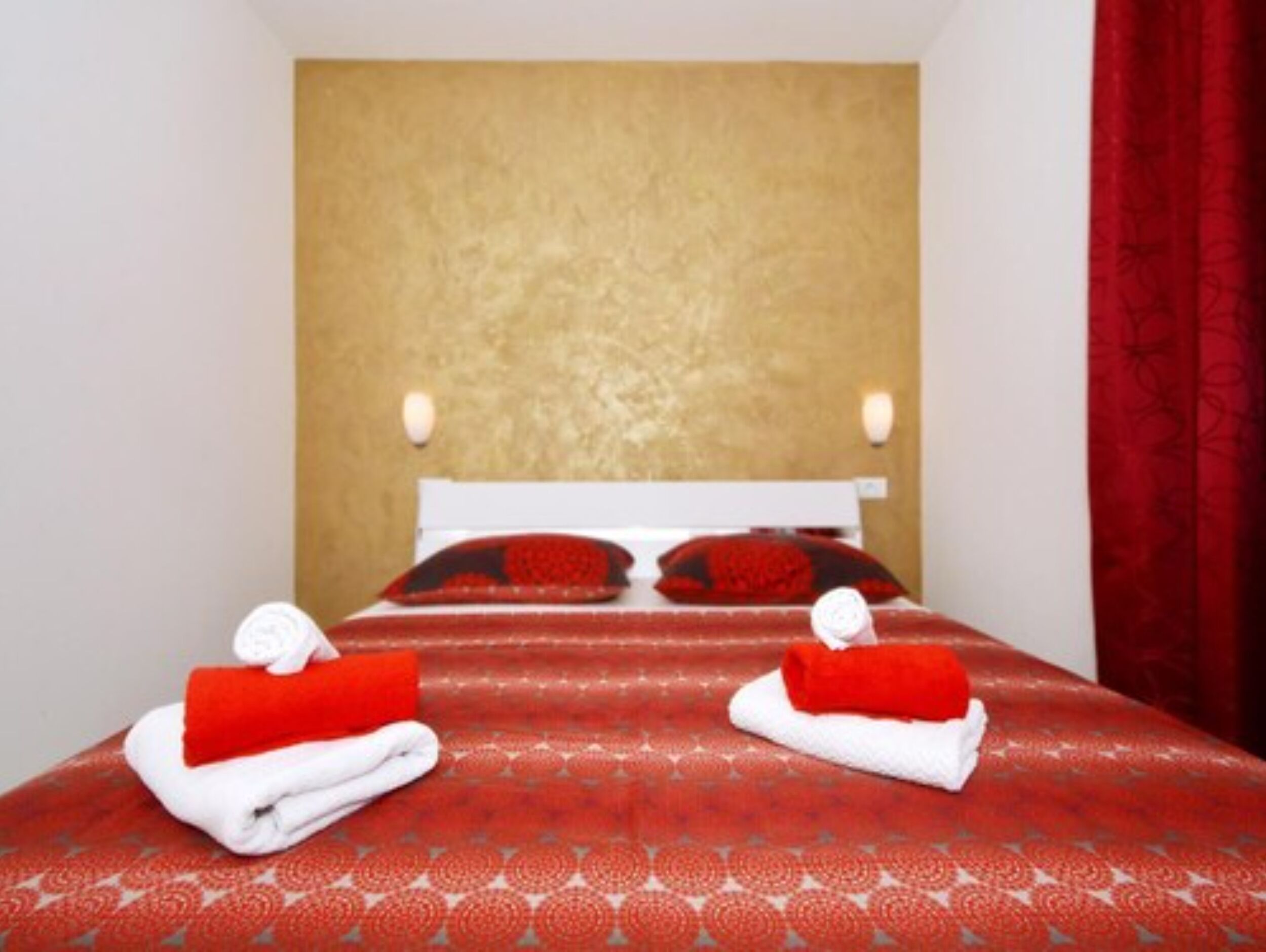 A hotel room with a bed, two towels, and a red curtain.