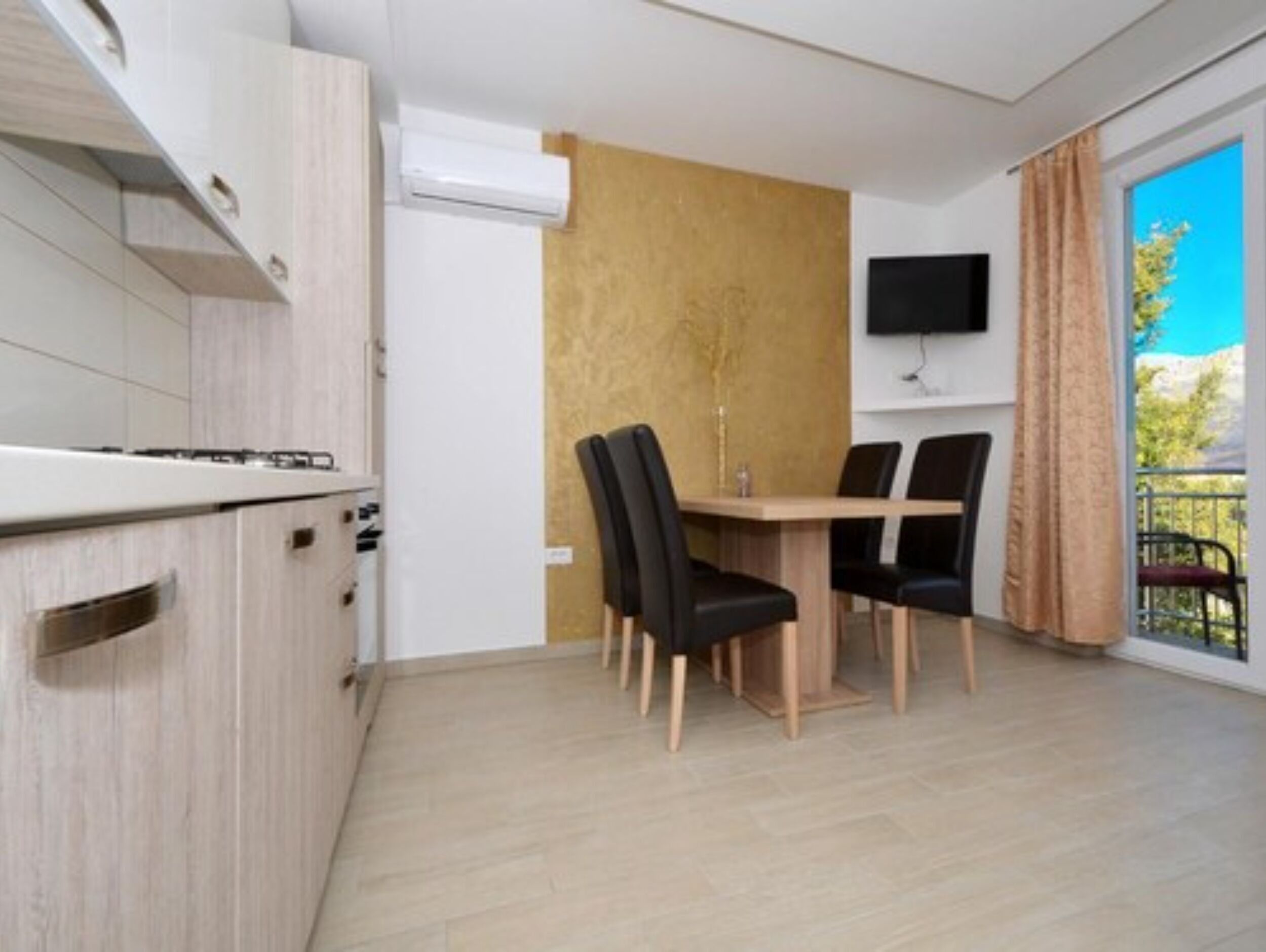 Een moderne keuken met een ingebouwde kookplaat, een eetgedeelte met een houten tafel en zwarte stoelen, en een groot raam met uitzicht op de omgeving.
