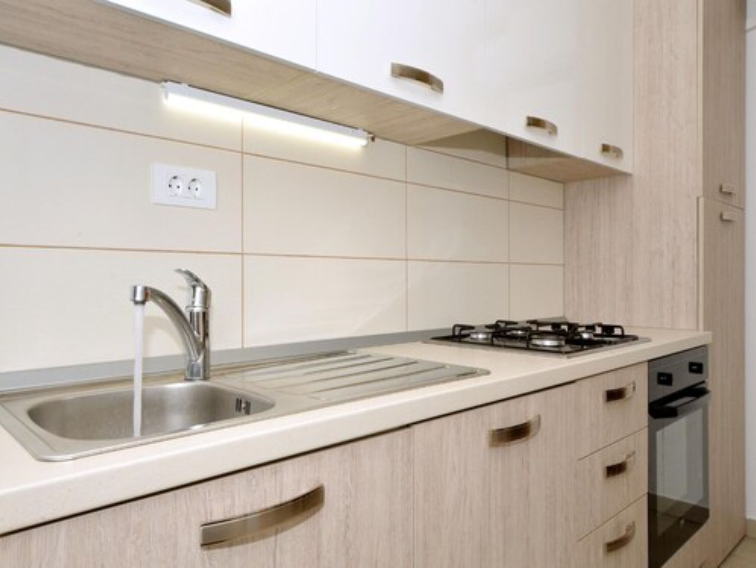 Una cocina moderna con un lavamanos de acero inoxidable, una estufa a gas y armarios de madera.