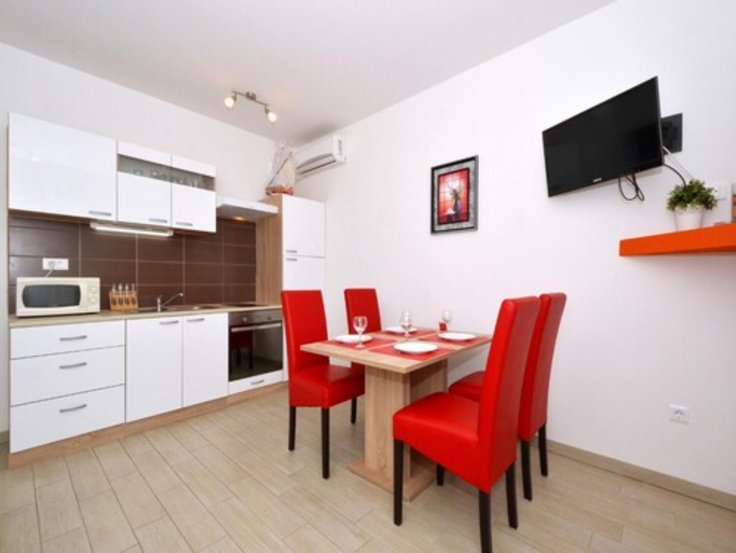 A modern kitchen with white cabinets, a microwave, and a dining area with red chairs and a wooden table.