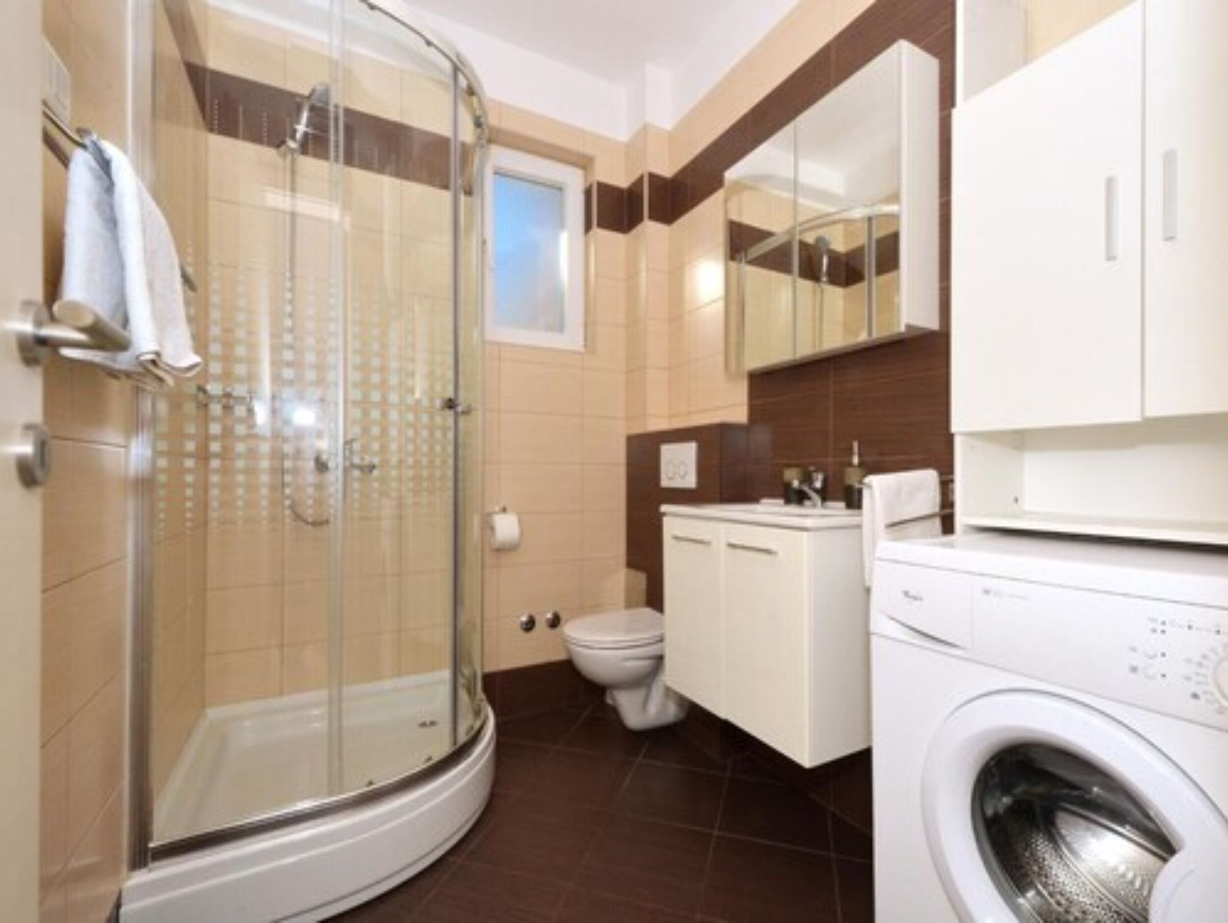 Une salle de bain moderne avec une douche à parois de verre, des toilettes, un lavabo et un lave-linge.