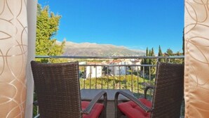 A balcony with wicker chairs and red cushions, overlooking a mountainous landscape. - Lobster Apartments (Split)