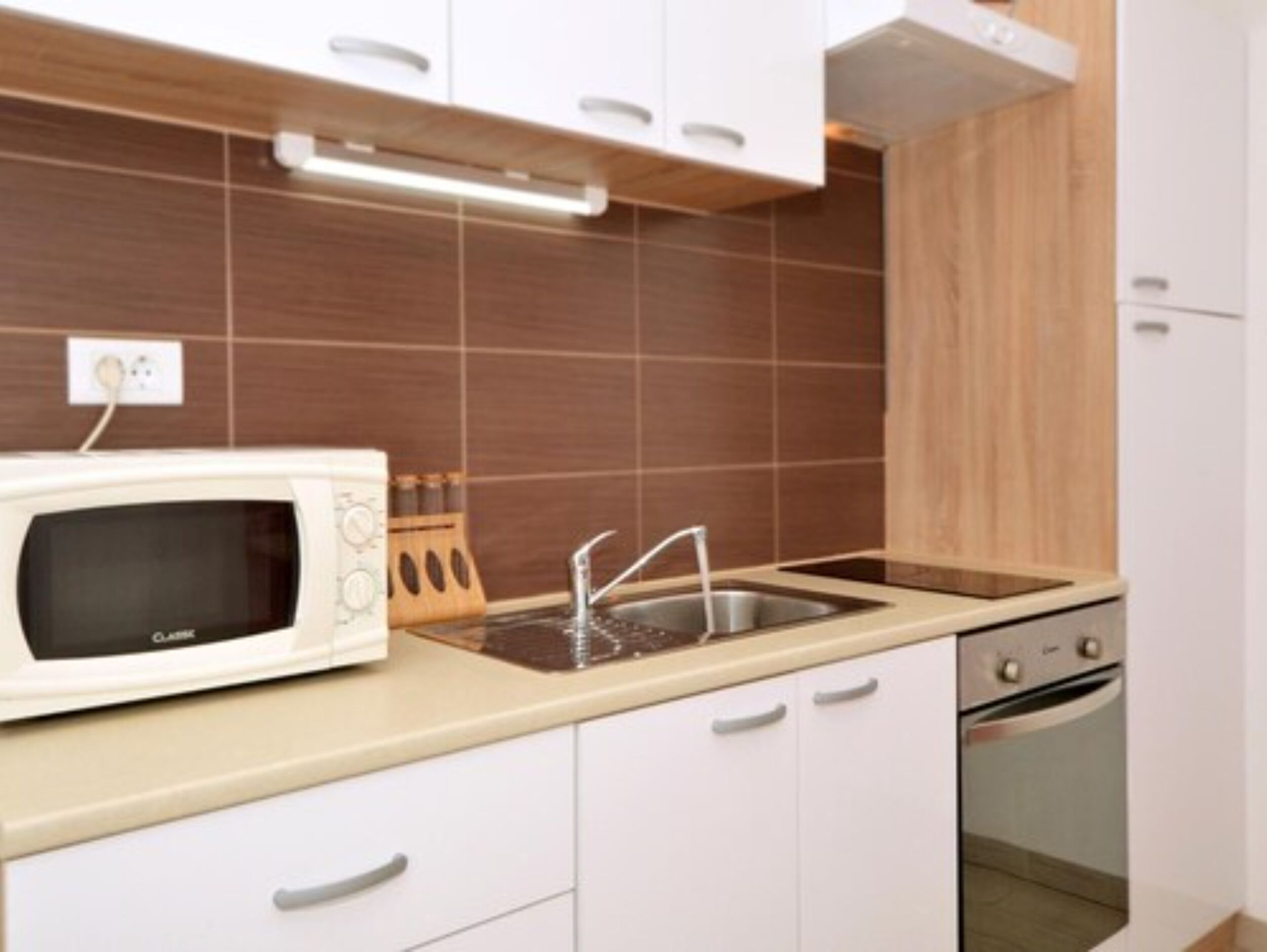 Eine Küche mit weißen Schränken, einer Mikrowelle, einem Spülbecken und einem Backofen.