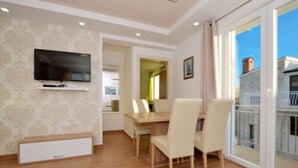 A modern dining area with a flat-screen TV mounted on the wall, a wooden table, and two chairs. - Lobster Apartments (Split)