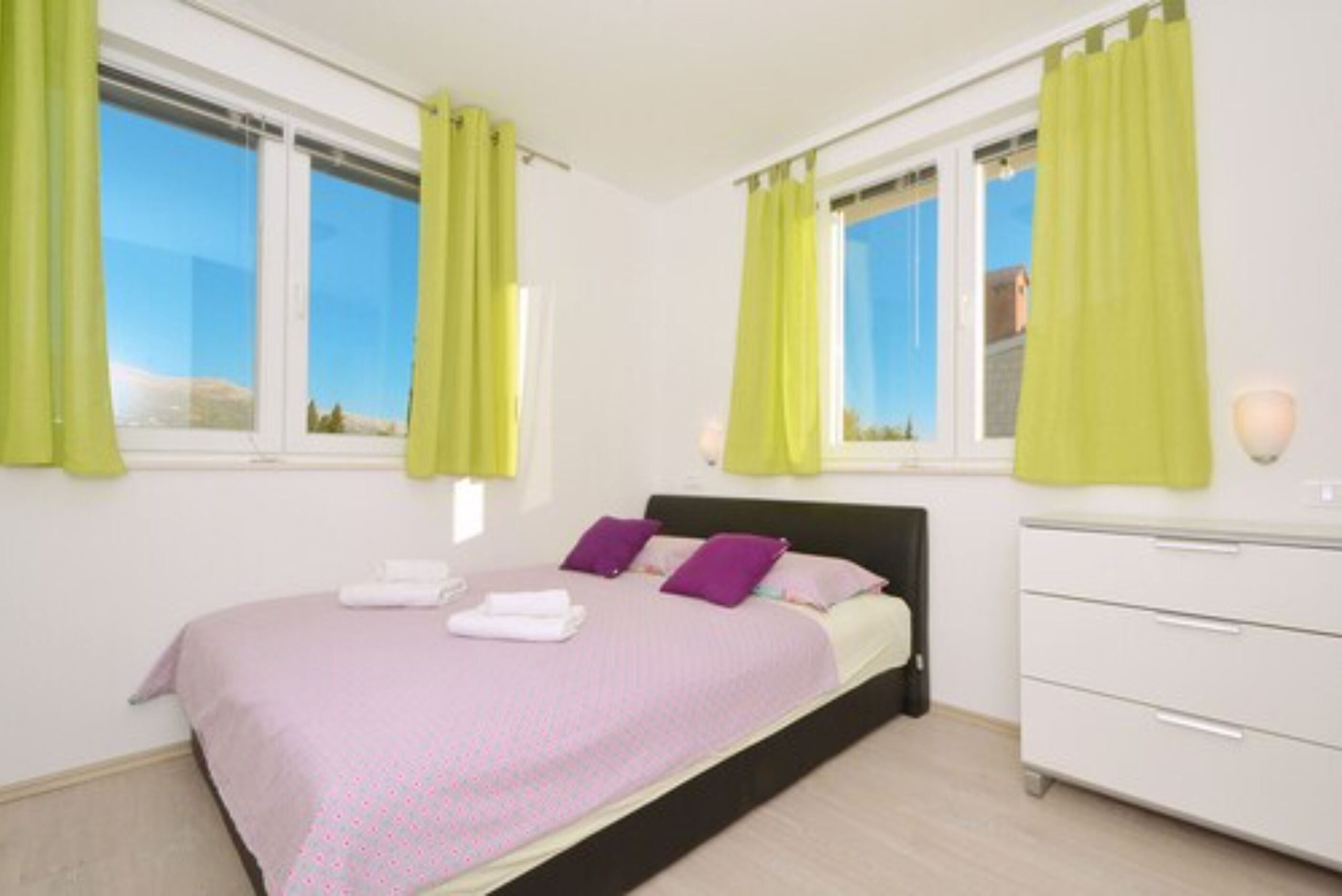 A bedroom with a bed, a dresser, and two windows with curtains.