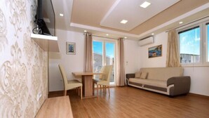 A modern living room with a wooden floor, a sofa, a dining table with chairs, and a TV mounted on the wall. - Lobster Apartments (Split)