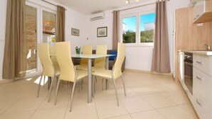 A dining area with a table and chairs, a window with curtains, and a kitchen area with cabinets. - Lobster Apartments (Split)
