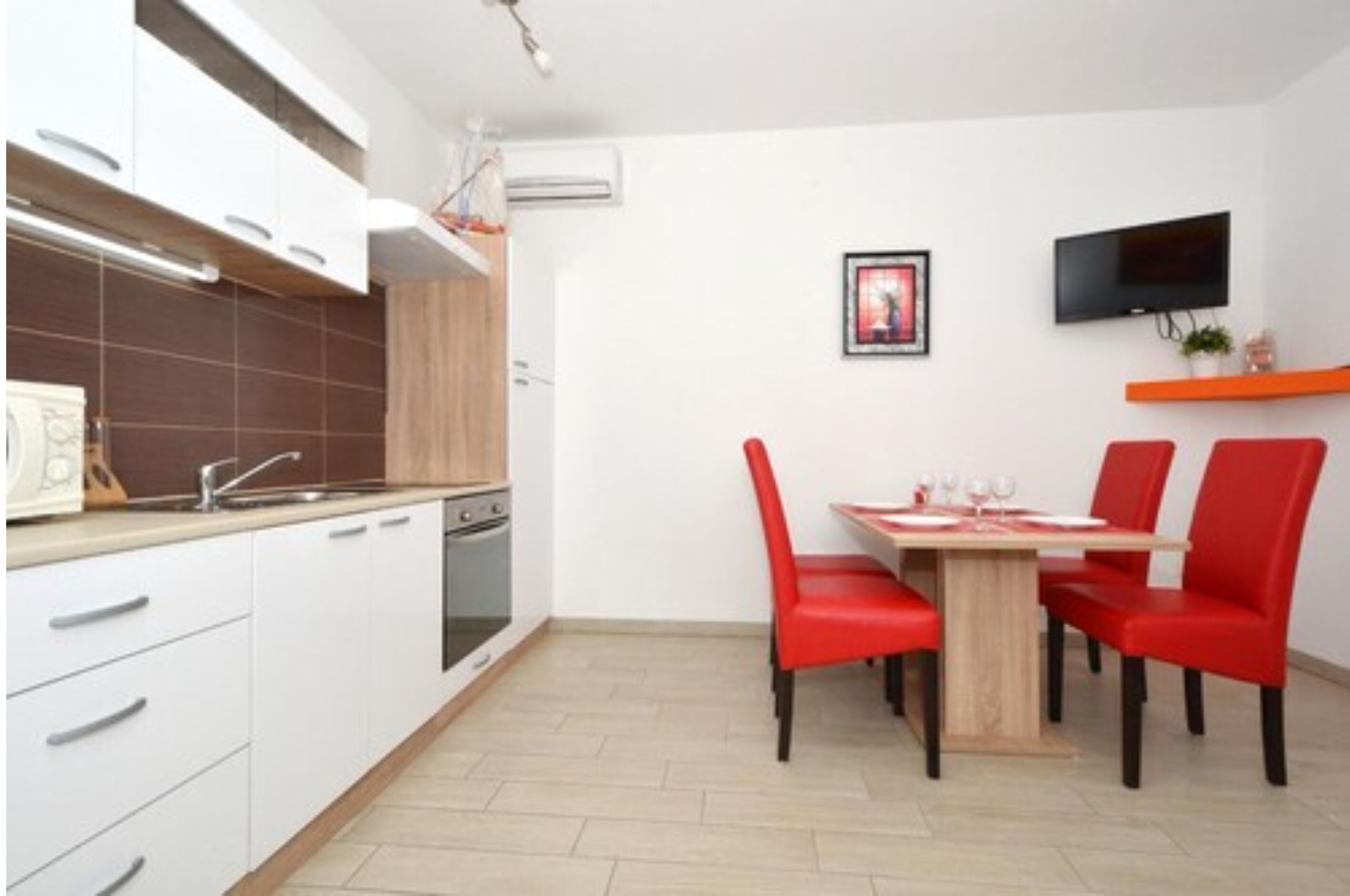 A modern kitchen with white cabinets, a wooden countertop, and a dining area with a wooden table and red chairs.