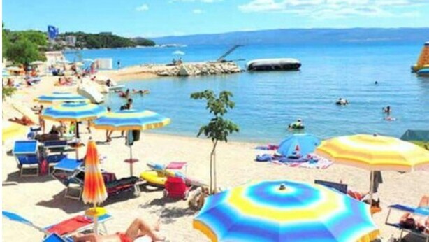 A beach with multiple umbrellas, sun loungers, and people enjoying the water. - Lobster Apartments (Split)