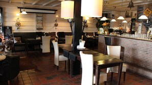 A restaurant with a brick wall, wooden tables, and chairs. There is a bar area with a counter and glasses.