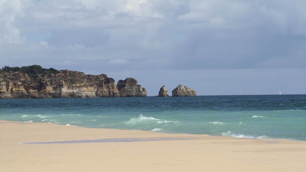 A beach with clear turquoise water, sandy shore, and rocky cliffs in the background. - Beautiful 2 Bed Top Floor Apt  on Oasis Parque, Alvor (Portimão)