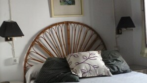 Un dormitorio con cama, mesita de noche, lámpara de pared y un cuadro en la pared.