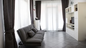 Un salon moderne avec un canapé gris, des meubles blancs et une grande fenêtre agrémentée de rideaux.