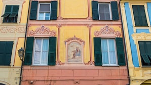 Un immeuble à plusieurs étages, doté de détails architecturaux élaborés, notamment une fresque centrale et des volets verts aux fenêtres.