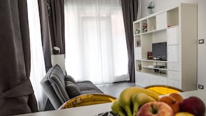 Un salon moderne avec un canapé, un meuble de rangement blanc pour appareils électroniques et un panier de fruits sur la table.