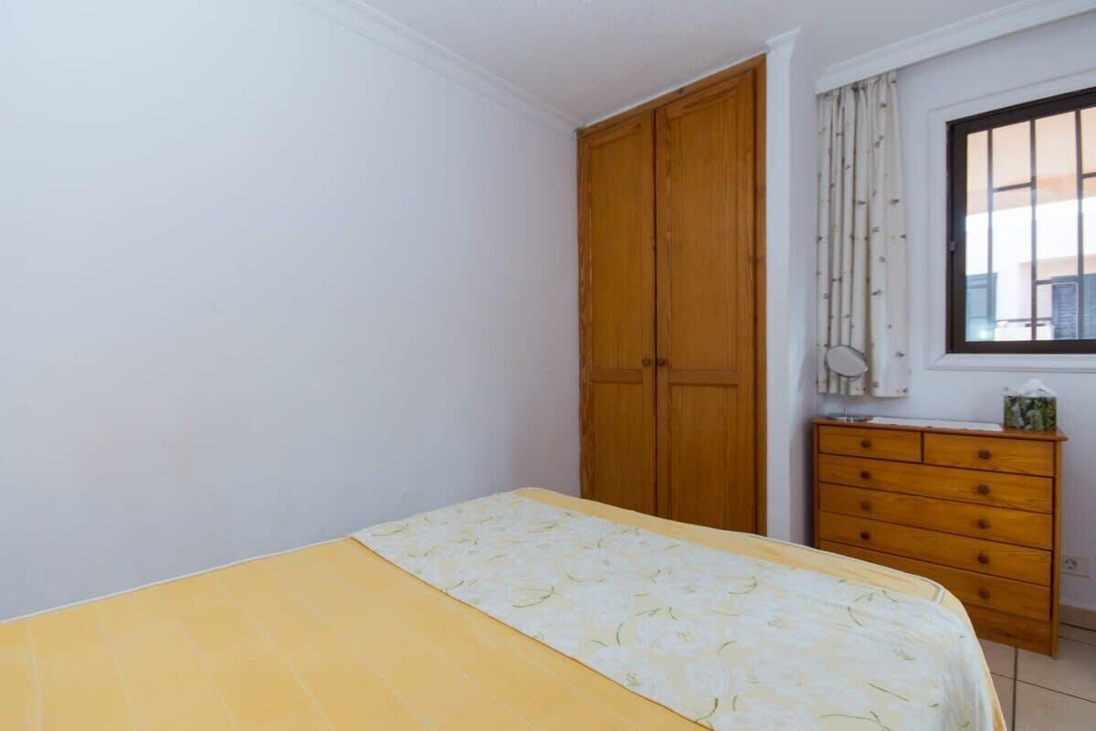 A bedroom with a bed, a wardrobe, a dresser, and a window with curtains.