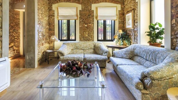 A spacious living room with stone walls and a high ceiling, featuring a glass coffee table and two sofas. - Villas Marim Flamingo Villa (Olhão)