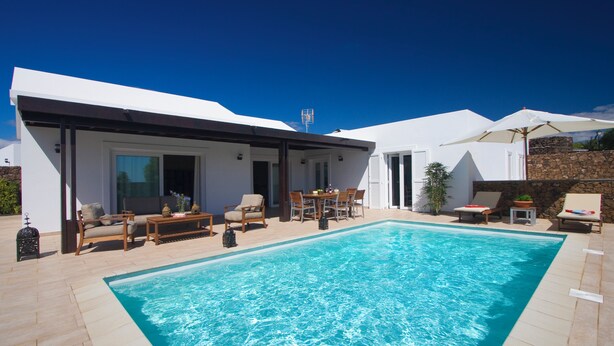 Un área de piscina moderna con piscina rectangular, mobiliario exterior y un porche cubierto.